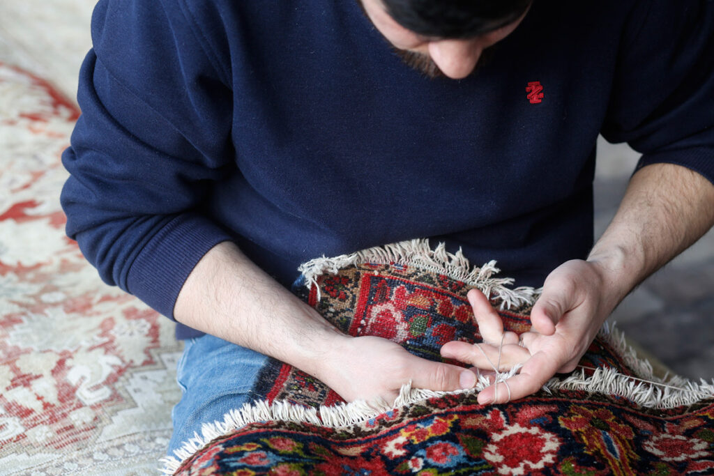 Individual repairing an Oriental rug, focusing on reweaving frayed edges